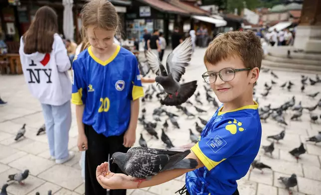 Children in Bosnian national soccer team jerseys feed pigeons in the old part of Sarajevo ahead of the soccer match of the FIFA World Cup 2026 between Canada and Bosnia, in Sarajevo, Bosnia, Friday, June 12, 2026. (AP Photo/Armin Durgut)