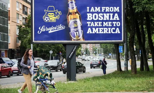 A woman walks past a billboard displaying lyrics from the Dubioza kolektiv song "I Am From Bosnia, Take Me to America" in Sarajevo, Bosnia, Thursday, June 11, 2026. (AP Photo/Armin Durgut)