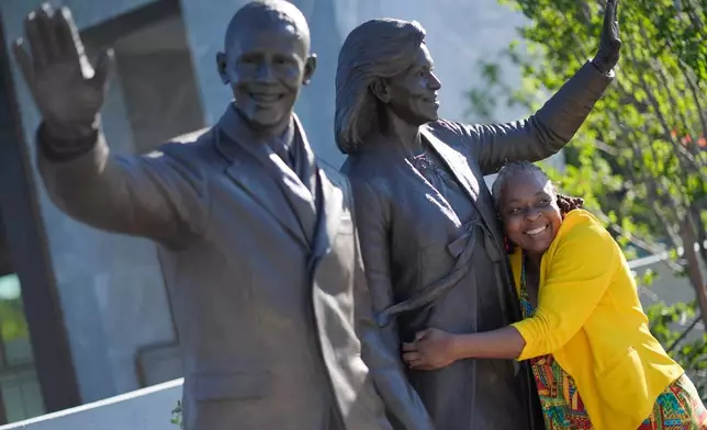 Sonya Hankerson, from Ft. Lauderdale, Fla., hugging the statue of former President Barack Obama and former first lady Michelle Obama as she visits the Obama Presidential Center on the official opening, Friday, June 19, 2026 in Chicago. (AP Photo/Pablo Martinez Monsivais)