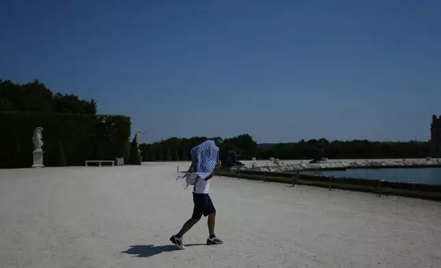 A man shields himself from the sun with a scarf as he walks in the garden of the Palace of Versailles, outside Paris, during a heat wave with temperatures soaring above 40 degrees Celsius (104 Fahrenheit), Monday, June 22, 2026. (AP Photo/Thibault Camus)