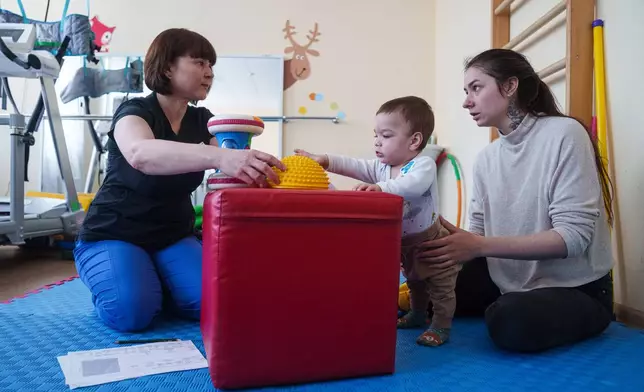 Marharyta Nekhoroshyva, right, speaks to a medic while her son Mark plays with toys during a therapy session at the children's regional hospital in Zaporizhzhia, Ukraine, Thursday, May 7, 2026. (AP Photo/Evgeniy Maloletka)