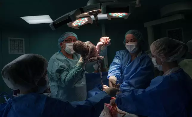 A doctor holds a newborn girl, Diana, after performing a cesarean section on her mother, Olha Karpenko, at the regional perinatal center of Zaporizhzhia, Ukraine, Wednesday, May 6, 2026. (AP Photo/Evgeniy Maloletka)