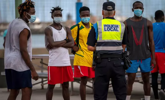 FILE - A police officer speaks with migrants and asylum-seekers in Gran Canaria island, Spain, Tuesday, Aug. 18, 2020. (AP Photo/Emilio Morenatti, File)