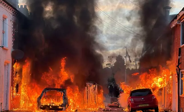 Vehicles set on fire by protesters burn on Lendrick Street in east Belfast, Northern Ireland, on Tuesday, June 9, 2026, after the arrest of a Sudanese man accused of stabbing a man in the northern part of the city. (PA via AP)