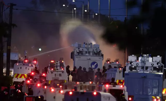 Police fire a water cannon towards rioters after they set fire to wheelie bins and removed a garden fence to use as a shield against the water cannon in Newtownabbey, Belfast, Northern Ireland, Wednesday June 10, 2026. (PA via AP)