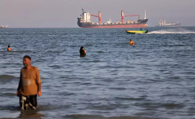 Residents swim in the waters of the Strait of Hormuz as a small motorboat passes cargo ships and other commercial vessels offshore near Bandar Abbas, Iran, Wednesday, June 17, 2026. (Amirhosein Khorgooi/ISNA via AP)