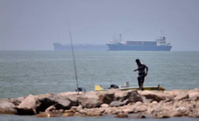 A man stands beside a fishing pole along the shore as cargo ships and commercial vessels are seen in the Strait of Hormuz off Bandar Abbas, Iran, Wednesday, June 17, 2026. (Amirhosein Khorgooi/ISNA via AP)