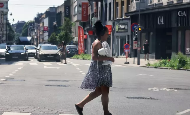 A woman walks across the street with a fan in her arms in the center of Brussels, Thursday, June 25, 2026. (AP Photo/Omar Havana)