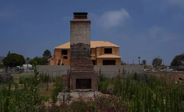 A chimney stands on a lot covered with weeds and wildflowers in front of a home under construction more than a year after the Palisades Fire in the Pacific Palisades neighborhood of Los Angeles, Thursday, June 4, 2026. (AP Photo/Jae C. Hong)