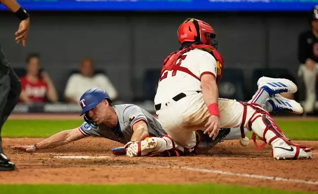 Texas Rangers' Evan Carter, left, scores behind Cleveland Guardians catcher Austin Hedges (27) in the ninth inning of a baseball game in Cleveland, Monday, June 29, 2026. (AP Photo/Sue Ogrocki)