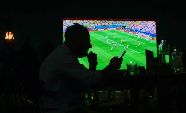 A man watches a World Cup Round of 32 match between Brazil and Japan, on his cell phone while sitting at a bar in Nicosia, Cyprus, Monday, June 29, 2026. (AP Photo/Petros Karadjias)
