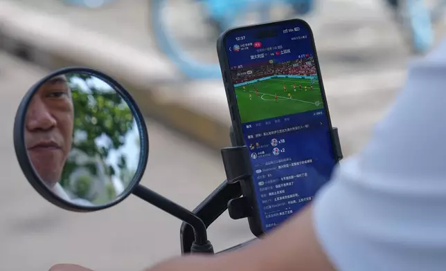 A rider watches a live broadcast of the World Cup Group D soccer match between Australia and Turkey via his smartphone clipped on his e-bike while riding on a street in Beijing, Sunday, June 14, 2026. (AP Photo/Andy Wong)