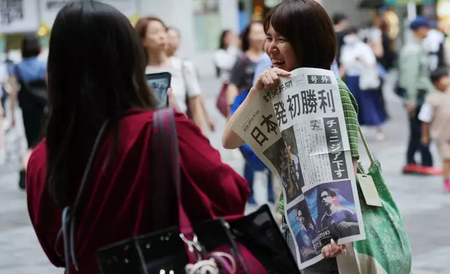 A woman poses for a photo with a copy of the extra handed out by Yomiuri Shimbun newspaper staff after Japan's team defeated Tunisia in their World Cup Group F soccer match in Mexico, in Tokyo, Sunday, June 21, 2026. (AP Photo/Hiro Komae)