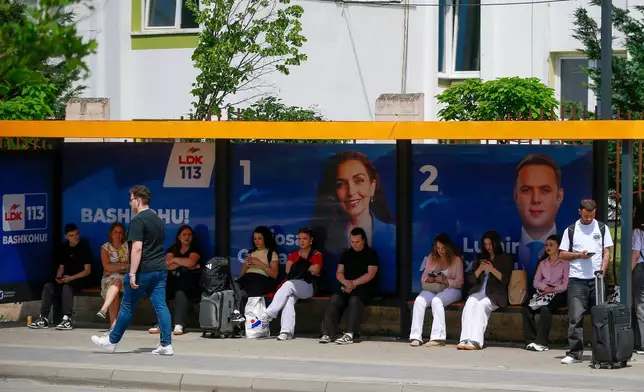 People wait at a bus station displaying election posters in capital Pristina, Kosovo, Friday, June 5, 2026, ahead of snap parliamentary elections on June 7. (AP Photo/Visar Kryeziu)