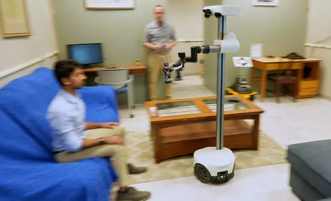 A robot operated by a robotics engineer, rear, brings a drink to colleague during a demonstration at the University of New Hampshire, Tuesday, April 21, 2026, in Durham, N.H. (AP Photo/Robert F. Bukaty)