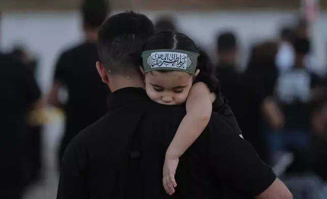 A girl wearing an Ashoura headband rests on her father's shoulder during a sermon marking the third day of Ashoura, the Shiite Muslim commemoration of the 7th-century death of Imam Hussein, the grandson of the Prophet Muhammad, in the southern port city of Tyre, Lebanon, Friday, June 19, 2026. (AP Photo/Hassan Ammar)