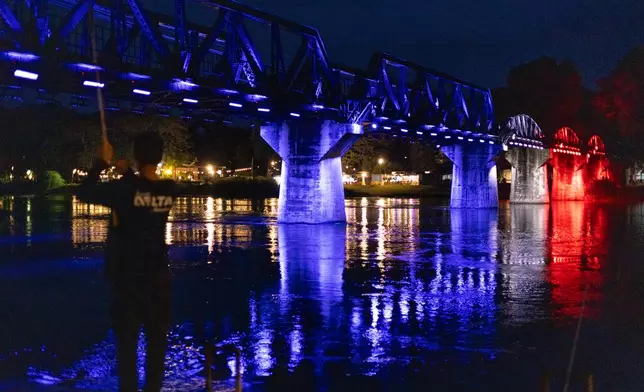 A man fishes in front of the River Kwai Bridge, one of the most iconic sections of the infamous World War II "Death Railway," as the bridge is lit up in the colors of the Thai flag in Kanchanaburi City, Thailand, Saturday, May 30, 2026. (AP Photo/Anton L. Delgado)