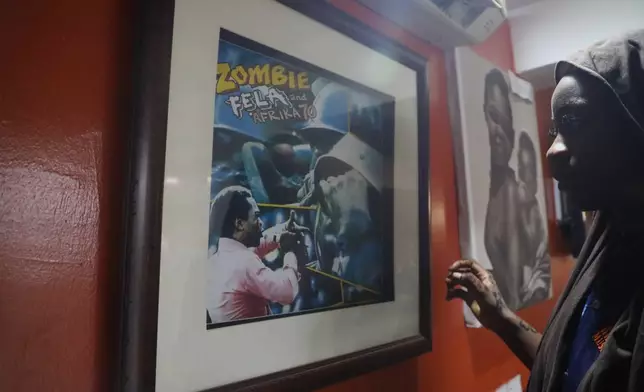 Qawiyat Omizi, a tour guide stand in front of a frame of Fela Kuti's Zombie at Kalakuta Museum in Lagos, Nigeria. Saturday, May 30, 2026. (AP Photo/Mansur Ibrahim)