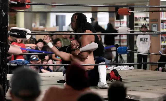 Fans watch as wrestler Elliot Rey, middle top, applies a hold on TJ Black during a Lucha Libro pro wrestling event at Benicia Public Library Saturday, May 2, 2026, in Benicia, Calif. (AP Photo/Jeff Chiu)