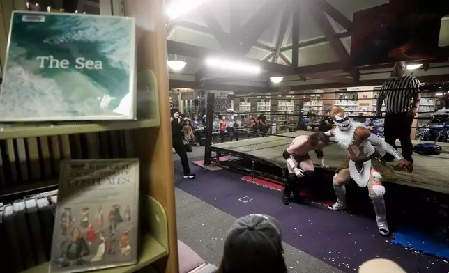 Wrestlers Jiah "the Crazy Cajun" Jewell, middle left, and El Chupacabra compete near book shelves at a Lucha Libro pro wrestling event at Benicia Public Library Saturday, May 2, 2026, in Benicia, Calif. (AP Photo/Jeff Chiu)