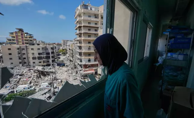 A nurse looks through a shattered window of the Jabal Amel Hospital into a destroyed building that was hit Monday in an Israeli airstrike, in the southern port city of Tyre, Lebanon, Tuesday, June 2, 2026. (AP Photo/Mohammed Zaatari)