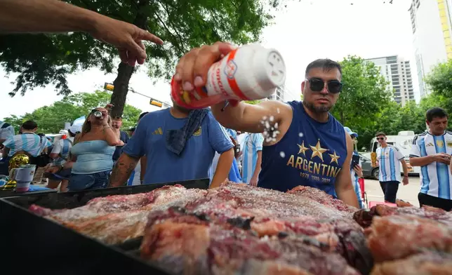 Lucas Martinez, of Dallas, an Argentina supporter, seasons meat with salt while grilling during a rally ahead of their team's World Cup Group J soccer match against Austria, Sunday, June 21, 2026, in Dallas. (AP Photo/Julio Cortez)