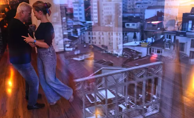 A city landscape is reflected in a window as people dance tango during a training session at 333 in Istanbul, Turkey, Sunday, Jan. 11, 2026. (AP Photo/Francisco Seco)
