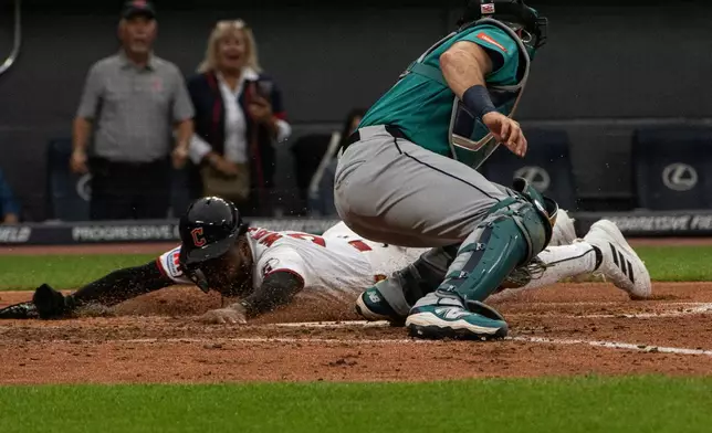 Seattle Mariners' Cal Raleigh, front, is late with the tag as Cleveland Guardians' Kahil Watson, left, slides safely into home plate on an RBI single by Guardians' Cooper Ingle during the third inning of a baseball game, Saturday, June 27, 2026, in Cleveland. (AP Photo/Phil Long)