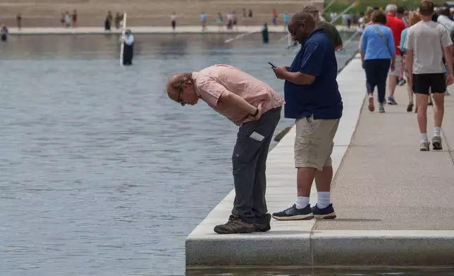 Visitors look into the Lincoln Memorial Reflecting Pool as National Park Service employees work in the background,Sunday, June 21, 2026, on the National Mall in Washington. (AP Photo/Jon Elswick)