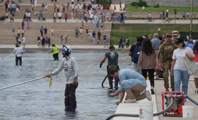 A visor takes a photo as National Park Service employees work to clean the Lincoln Memorial Reflecting Pool Sunday, June 21, 2026, on the National Mall in Washington. (AP Photo/Jon Elswick