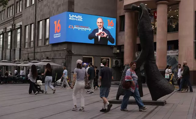 People walk along a street near a campaign advertisement for Armenian Prime Minister Nikol Pashinyan in Yerevan, Armenia, on Thursday, June 4, 2026. (AP Photo/Anthony Pizzoferrato)