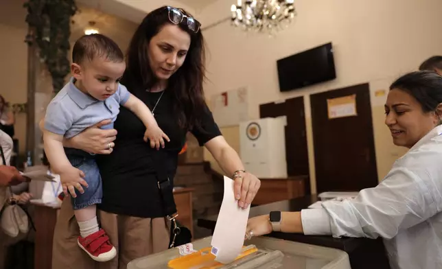 A woman holding a child casts her ballot at a polling station during a parliamentary election in Yerevan, Armenia, Sunday, June 7, 2026. (AP Photo/Anthony Pizzoferrato)