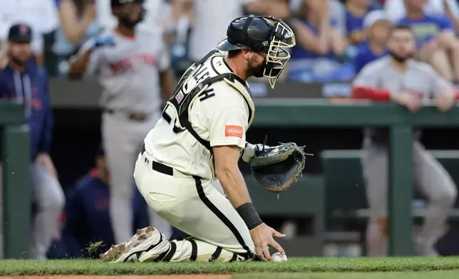Seattle Mariners catcher Cal Raleigh picks up the ball after a scoring play by the Boston Red Sox during the seventh inning of a baseball game, Friday, June 19, 2026, in Seattle. (AP Photo/John Froschauer)