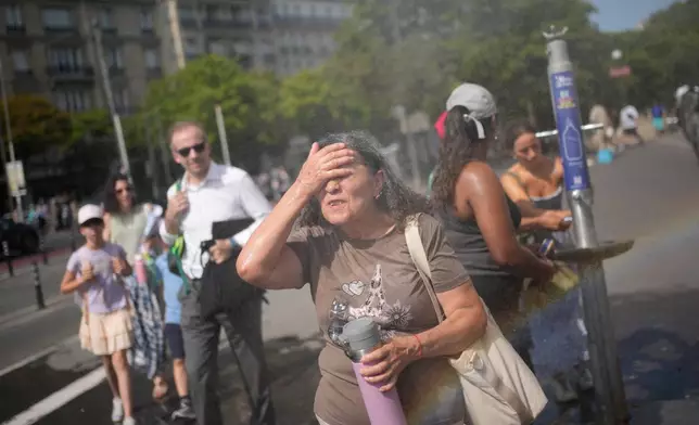 FILE - Tourists enjoy cooling off at a public water fountain In Paris, on June 26, 2026. (AP Photo/Christophe Ena, File)