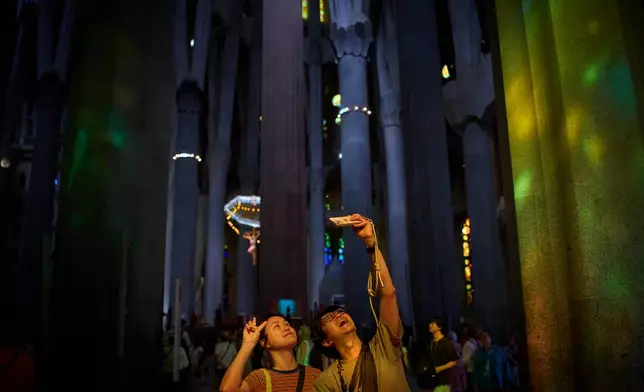 Visitors take photos inside Antoni Gaudí's Basilica of the Sagrada Familia as colored light from its stained-glass windows illuminates the interior in Barcelona, Spain, Tuesday, May 26, 2026, ahead of Pope Leo XIV's visit to the city in June. (AP Photo/Emilio Morenatti)