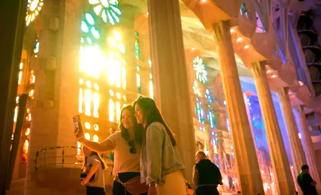 Visitors take photos inside Antoni Gaudí's Sagrada Família basilica as colored light from its stained-glass windows illuminates the interior in Barcelona, Spain, Wednesday, May 20, 2026, ahead of Pope Leo XIV's visit to the city in June. (AP Photo/Emilio Morenatti)
