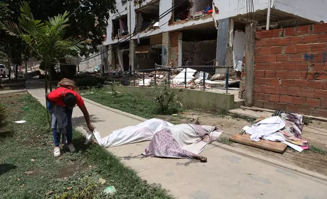 A man looks at covered bodies in front of a damaged building the day after earthquakes and several aftershocks struck La Guaira, Venezuela, Thursday, June 25, 2026. (AP Photo/Pedro Mattey)