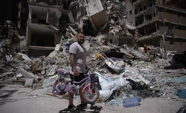 Barber Wissam Srour, 41, holds his daughter's bicycle recovered from his barbershop as he searches for belongings in the rubble of the shop, damaged in an Israeli strike, in the southern port city of Tyre, Lebanon, Friday, June 19, 2026. (AP Photo/Hassan Ammar)
