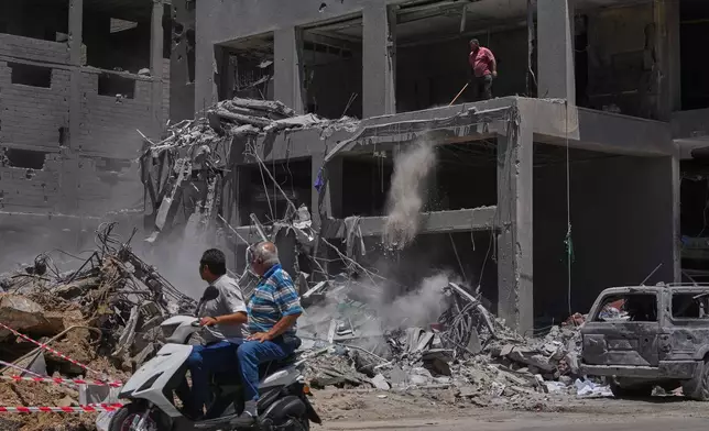 A man clears debris from a building damaged in an Israeli strike as two men ride past on a scooter in the southern port city of Tyre, Lebanon, Friday, June 19, 2026. (AP Photo/Hassan Ammar)