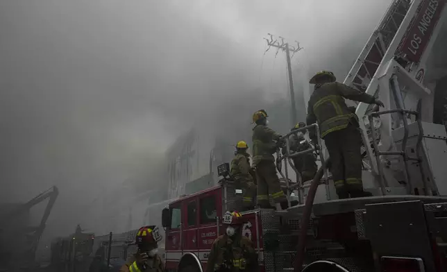 Firefighters work from a ladder truck while fighting a warehouse fire in the Boyle Heights neighborhood of Los Angeles, Sunday, June 21, 2026. (AP Photo/Jae C. Hong)