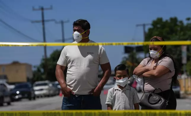 People wear masks while watching firefighters fight a warehouse fire in the Boyle Heights neighborhood of Los Angeles, Sunday, June 21, 2026. (AP Photo/Jae C. Hong)