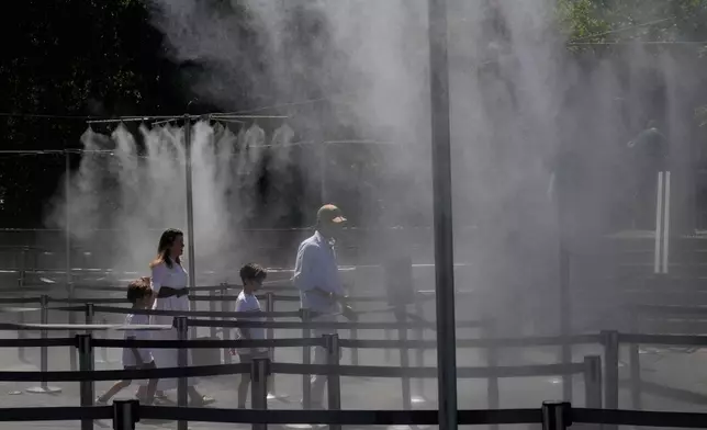 A family walks through a cooling water spray at the Eiffel Tower in Paris, Sunday, June 21, 2026. (AP Photo/Michel Euler)