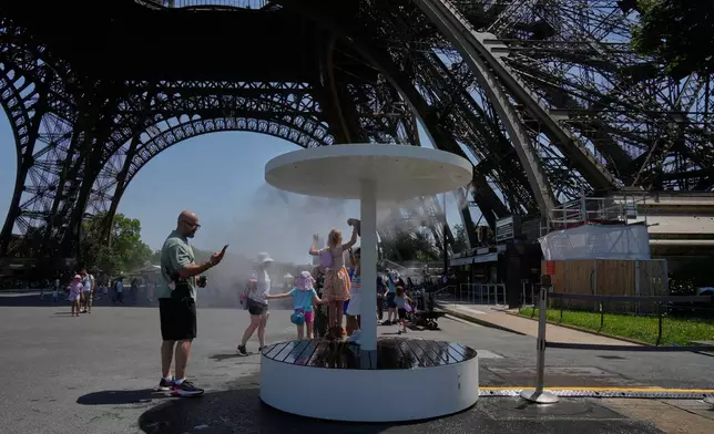 People cool off in a water spray at the Eiffel Tower in Paris, Sunday, June 21, 2026. (AP Photo/Michel Euler)