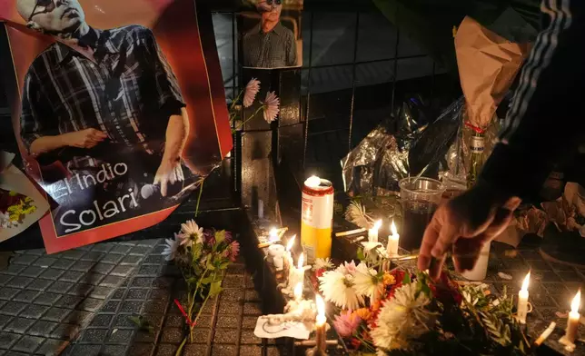 A person lights a candle near a picture of Carlos Alberto Solari, the Argentine singer-songwriter known as "the Indio" who led Patricio Rey y sus Redonditos de Ricota, on the day of his death, at Plaza de Mayo square in Buenos Aires, Argentina, Friday, June 5, 2026. (AP Photo/Gustavo Garello)
