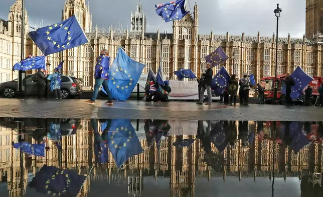 FILE - Protestors are reflected in a large puddle as they wave European flags to demonstrate against Brexit in front of the Parliament in London, Dec. 3, 2018. (AP Photo/Frank Augstein, File)
