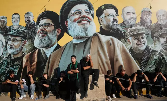 Hezbollah supporters sit in front of a giant billboard, that shows the two late hezbollah leaders Sayyed Hassan Nasrallah and Hashem Safieddine, centre, with other Hezbollah killed commanders, as they listen to the death story of Imam Hussein during the holy day of Ashoura in Dahiyeh, Beirut's southern suburbs, Lebanon, Friday, June 26, 2026. (AP Photo/Hussein Malla)