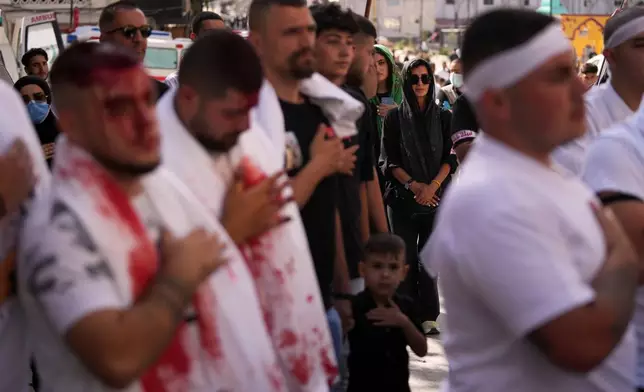 A woman watches as Lebanese Shiites beat their chests and bleed from self-inflicted ceremonial head wounds during Ashoura, when Shiites commemorate the martyrdom of Imam Hussein, the grandson of the Prophet Muhammad, amid buildings destroyed by Israeli strikes in Nabatiyeh, southern Lebanon, Friday, June 26, 2026. (AP Photo/Hassan Ammar)