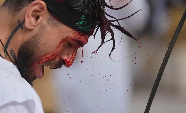 EDS NOTE: GRAPHIC CONTENT - A man bleeds from a ceremonial head wound as he strikes his head during Ashoura, when Shiites commemorate the martyrdom of Imam Hussein, the grandson of the Prophet Muhammad, amid buildings destroyed by Israeli strikes in Nabatiyeh, southern Lebanon, Friday, June 26, 2026. (AP Photo/Hassan Ammar)
