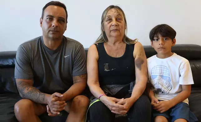 Grian Serrano, left, his mother, Ingrid Rochabrun, and his son, Gael, sit at the home where they are staying with relatives in Caracas, Venezuela, after surviving the back-to-back earthquakes that destroyed their apartment building in Caraballeda, Monday, June 29, 2026. Serrano also survived the 1999 mudslides that struck La Guaira. (AP Photo/Pedro Mattey)