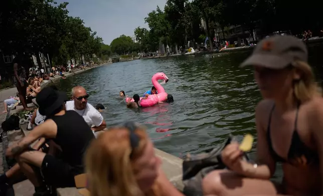 Parisians bath in the Canal Saint-Martin in Paris, as the national weather service, Meteo France, placed 54 departments, about half the country, under a red heat wave alert, Tuesday, June 23, 2026. (AP Photo/Christophe Ena )